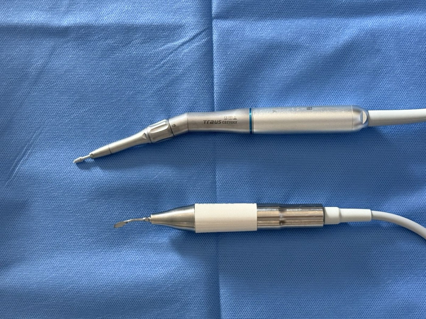 Two piezoelectric ultrasonic surgical handpieces with fine bone-cutting tips resting on a blue surgical drape